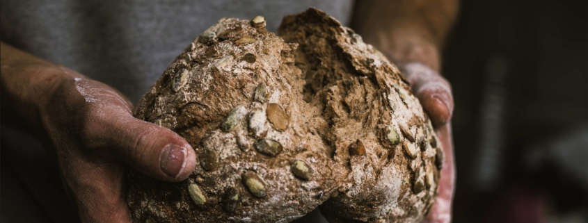 Hands breaking a loaf of seeded bread in half