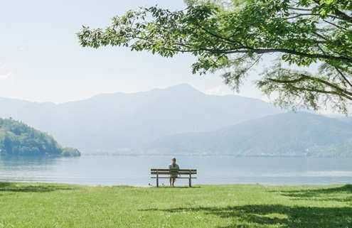 A person sits on a bench in an empty field, looking over the mountains