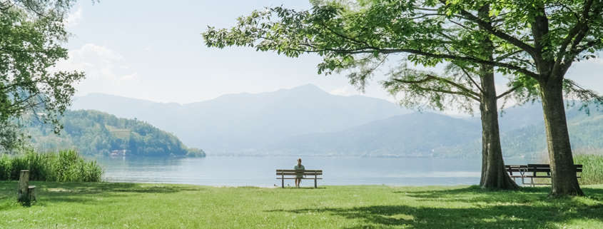 A person sits on a bench in an empty field, looking over the mountains