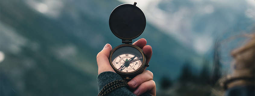 A compass is held up in front of mountains