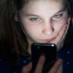 Young girl resting face on her hand and looking at a mobile phone which is lighting up her face.