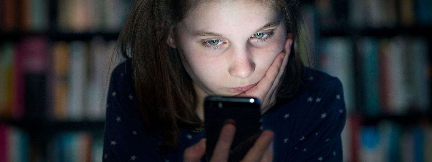 Young girl resting face on her hand and looking at a mobile phone which is lighting up her face.